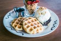 Waffles dusted with icing sugar and iceream and fruit on the side