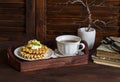 Waffles with honey and cream, a cup of tea in a vintage tray, a stack of old books on brown wooden table. Royalty Free Stock Photo