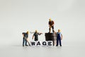 `WAGE` word in white cube. Miniature people and pile of coins.
