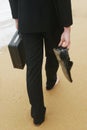 A waist-down shot of a lady walking bare feet on the beach holding a briefcase and her shoes. Conceptual image shot Royalty Free Stock Photo