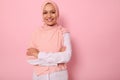 Waist-length portrait of a gorgeous Arabic Muslim woman in pink hijab posing looking to camera with attractive gaze, toothy smile