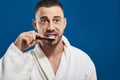 Waist up of Caucasian young man brushing his teeth against blue background Royalty Free Stock Photo