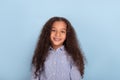 Waist up emotional portrait of mulatta frizzy girl wearing blue shirt against blue background in studio