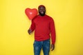 Waist up of happy African man keeping heart-shaped ballooon against yellow background Royalty Free Stock Photo