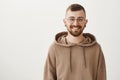 Waist-up indoor shot of friendly handsome hipster guy with trendy haircut and glasses smiling cheerfully while standing Royalty Free Stock Photo