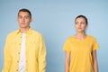 Waist up photo of a confused couple in yellow shirts looking at each other