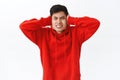 Waist-up portrait of annoyed, displeased asian man in red hoodie, telling neighbour turn volume down, shut ears