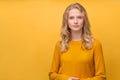 Waist up portrait of beautiful young serious clever blonde Scandinavian woman on bright yellow orange wall