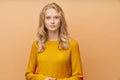 Waist up portrait of beautiful young serious clever blonde Scandinavian woman on bright yellow orange wall