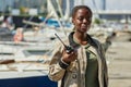 Black young woman holding radio and smiling at camera working in yacht docks