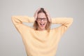 Waist-up portrait of blonde woman screaming, panicking, holding hands on head. wearing yellow sweater and glasses. poses against