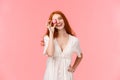 Waist-up portrait charismatic redhead female in white spring dress, tilt head and smiling carefree, holding macaron