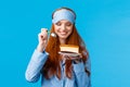 Waist-up portrait cheerful and delighted young caucasian redhead woman in pyjama and sleep mask, holding slice cake and