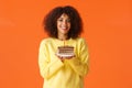 Waist-up portrait dreamy african-american b-day girl with afro haircut, holding plate with birthday cake and lit candle