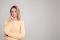 Waist-up portrait go young blonde woman smiling and biting her finger , looking aside. wearing yellow sweater. poses against grey Royalty Free Stock Photo