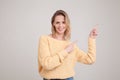 Waist-up portrait of happy smiling blonde woman pointing fingers away, showing something interesting and exiting, looking at the Royalty Free Stock Photo