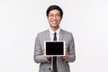 Waist-up portrait of pleased good-looking asian man in grey suit and glasses, introduce application, project or Royalty Free Stock Photo