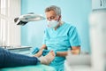 Chiropodist podiatrist in blue uniform and gloves with medical tool in hand while doing treatment procedure on feet