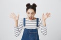 Portrait of surprised brunette girl in striped top and denim overall screaming in excitement, looking down. Cute female