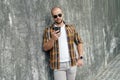 Waist up portrait of young good looking bold bearded guy standing outdoors against grey modern loft wall with call phone in his Royalty Free Stock Photo