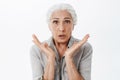 Waist-up shot of anxious and surprised kind grandmother feeling worried and amazed holding palms near face looking