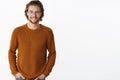 Waist-up shot of attractive pleasant bearded guy with earrings and long hair in glasses and warm sweater smiling