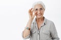 Waist-up shot of charming kind and nice granny in sight glasses touching rim of eyewear and smiling joyfully helping