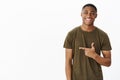 Waist-up shot of cheerful nice and handsome young african american man pointing left with index finger smiling and Royalty Free Stock Photo