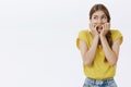 Waist-up shot of concerned nervous and anxious cute young timid woman in yellow t-shirt biting fingernails looking