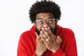 Waist-up shot of delighted happy african american male bearded friend in glasses chuckling, giggling with hand covering