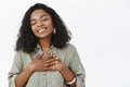 Waist-up shot of dreamy and touched tender African American girl with curly hairstyle holding palms on heart closing