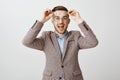 Waist-up shot of enthusiastic charming european male entrepreneur picking new glasses in optician store putting on round