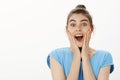 Waist-up shot of excited happy and cute female with bun hairstyle, grinning and gazing with impressed and surprised look