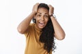 Waist-up shot of freaked out scared panicking cute african american young female screaming holding hands on head in Royalty Free Stock Photo