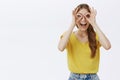 Waist-up shot of funny excited and creative happy caucasian girl with braid in yellow t-shirt making circles over eyes