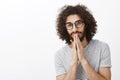 Waist-up shot of handsome dreamy hispanic male model with beard and afro hairstyle, holding hands in pray near mouth and