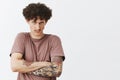 Waist-up shot of intense angry and young curly-haired man with moustache and tattoos holding offence inside Royalty Free Stock Photo
