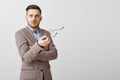 Waist-up shot of intense confused good-looking male entrepreneur in stylish jacket taking off glasses and gesturing with