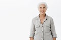 Waist-up shot of kind and cute energized grandmother with gray hair in casual shirt smiling broadly with happy