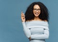 Waist up shot of mirthful Afro American woman holds smart phone, waits for call, enjoys pleasant conversation, has bushy curly