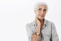 Waist-up shot of nostalgic and thoughtful wise cute senior woman with white hair touching neck gazing at upper left