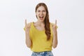 Waist-up shot of outgoing energized and excited attractive stylish woman in yellow t-shirt showing rock n roll sign