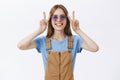 Waist-up shot of peaceful charming and charismatic good-looking female in sunglasses and brown overalls showing peace or