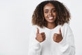 Waist-up shot of satisfied happy dark-skinned girl smiling broadly happily and showing thumbs up in like and support