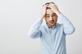 Waist-up shot of tired troubled good-looking young man with bristle pulling hair behind with hands on head frowning Royalty Free Stock Photo