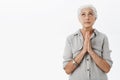 Waist-up shot of wise and cute grandmother praying for kids be heatlhy and safe holding hands in pray near chest looking