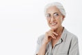 Waist-up shot of wise and pleased carefree kind grandmother in glasses with white hair holding hand on chin in