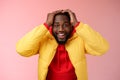 Waist-up surprised happy lucky young african-american bearded male in yellow jacket holding hands head smiling impressed