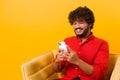 Waist up view of happy handsome blogger young adult man sitting at the armchair, using smartphone and texting message Royalty Free Stock Photo