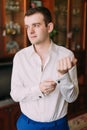 Waistup portrait of young smiling handsome businessman in suit putting cufflinks indoors and looking toward